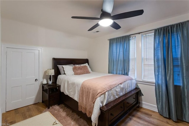 bedroom with wood finished floors, multiple windows, a ceiling fan, and baseboards