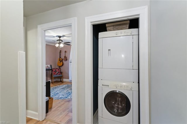 clothes washing area featuring estacked washer and dryer, light wood finished floors, and baseboards