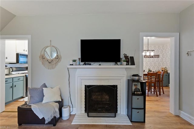 living room featuring a chandelier, light wood-style floors, a brick fireplace, and lofted ceiling