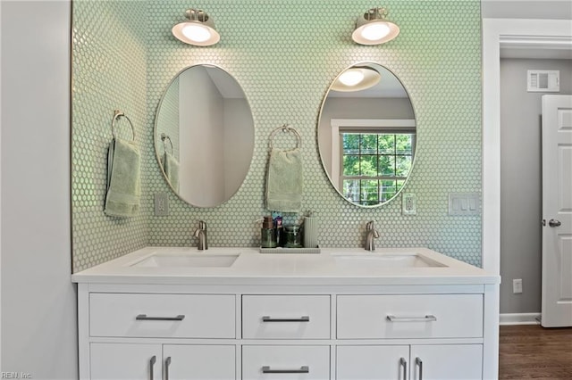 full bath with baseboards, wood finished floors, double vanity, and backsplash