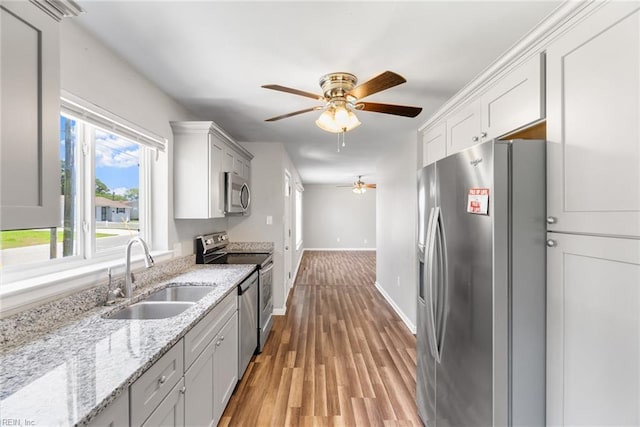 kitchen with appliances with stainless steel finishes, a sink, a ceiling fan, light wood-type flooring, and light stone countertops
