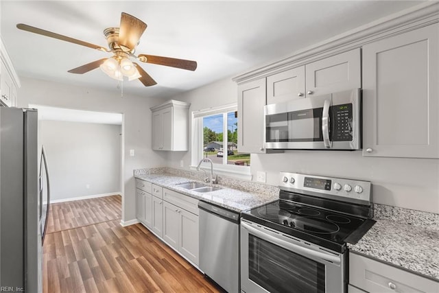kitchen with appliances with stainless steel finishes, a sink, ceiling fan, light wood-type flooring, and baseboards