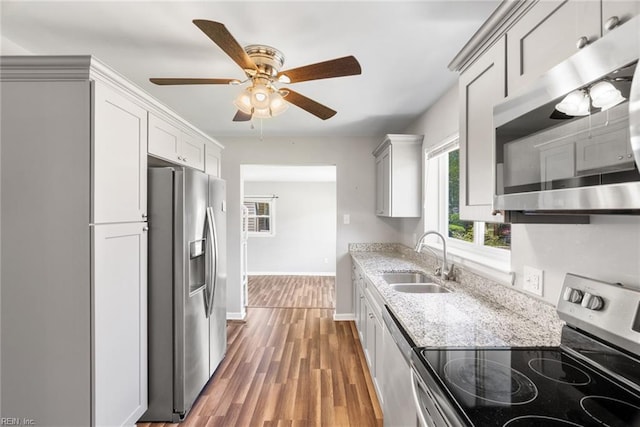 kitchen featuring stainless steel appliances, a sink, light stone countertops, ceiling fan, and light wood finished floors