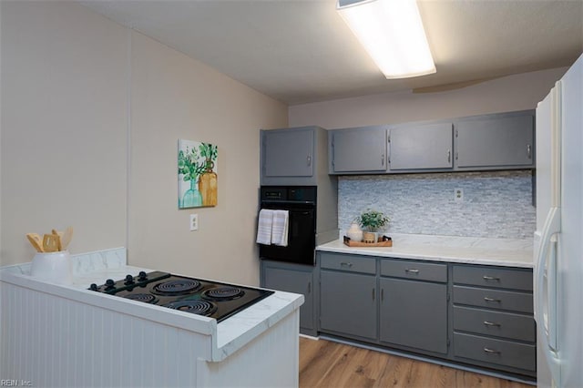 kitchen featuring gray cabinetry, black appliances, backsplash, and light wood-type flooring