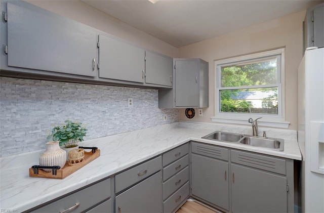 kitchen featuring gray cabinets, a sink, white refrigerator with ice dispenser, and decorative backsplash