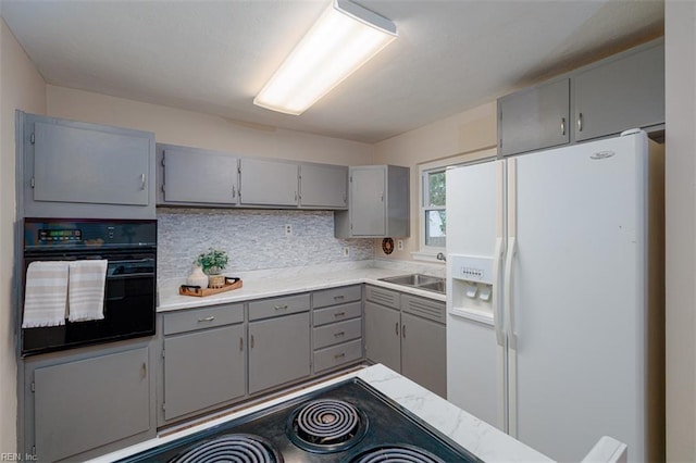 kitchen with gray cabinets, black oven, white refrigerator with ice dispenser, and a sink