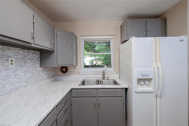 kitchen with white refrigerator with ice dispenser, gray cabinets, backsplash, a sink, and light countertops