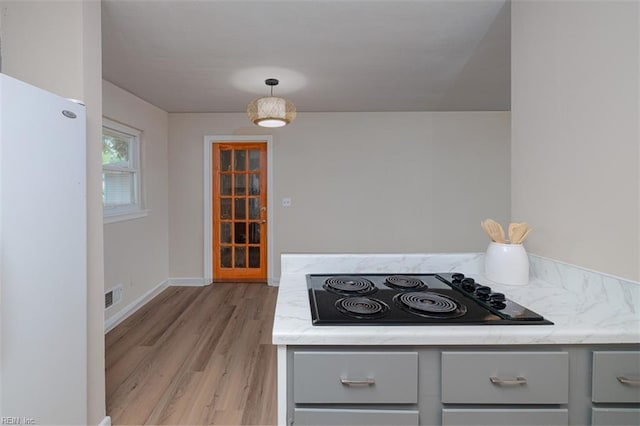 kitchen featuring freestanding refrigerator, black electric stovetop, gray cabinetry, light wood-style flooring, and light stone counters