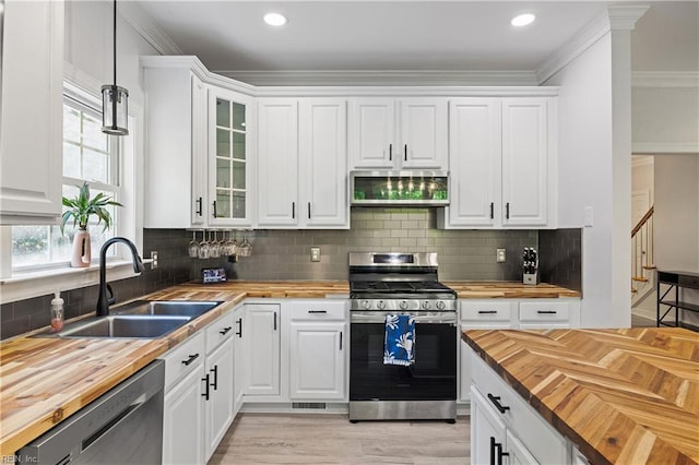 kitchen featuring wooden counters, appliances with stainless steel finishes, a sink, decorative light fixtures, and white cabinetry