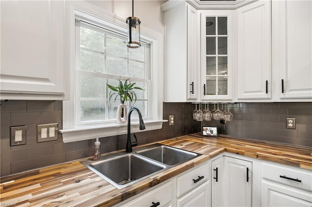 kitchen with butcher block countertops, a sink, white cabinetry, and glass insert cabinets
