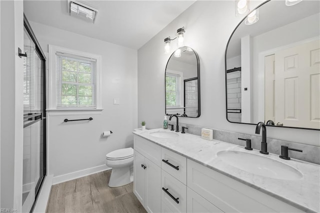 full bathroom featuring wood finished floors, a shower with shower door, double vanity, toilet, and baseboards