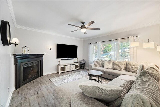 living room with ceiling fan, wood finished floors, a glass covered fireplace, baseboards, and ornamental molding