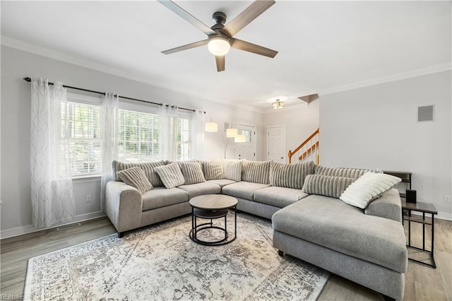 living area with a ceiling fan, wood finished floors, crown molding, baseboards, and stairs