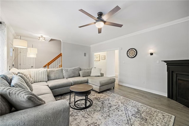 living area featuring ornamental molding, wood finished floors, a ceiling fan, baseboards, and a fireplace