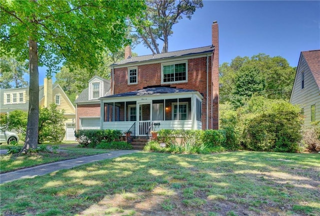 traditional-style home featuring a chimney, a front lawn, brick siding, and a porch
