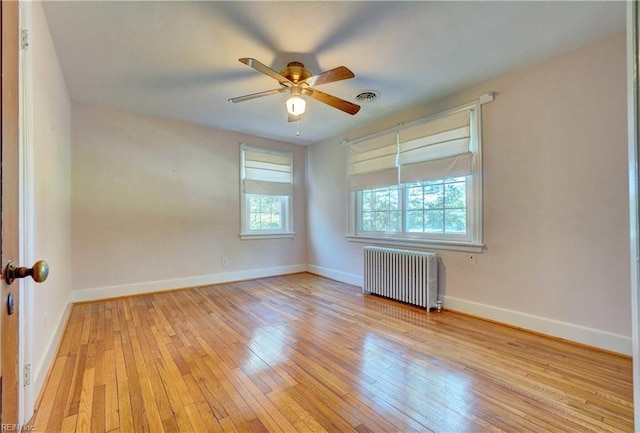 empty room with radiator, light wood-type flooring, ceiling fan, and baseboards