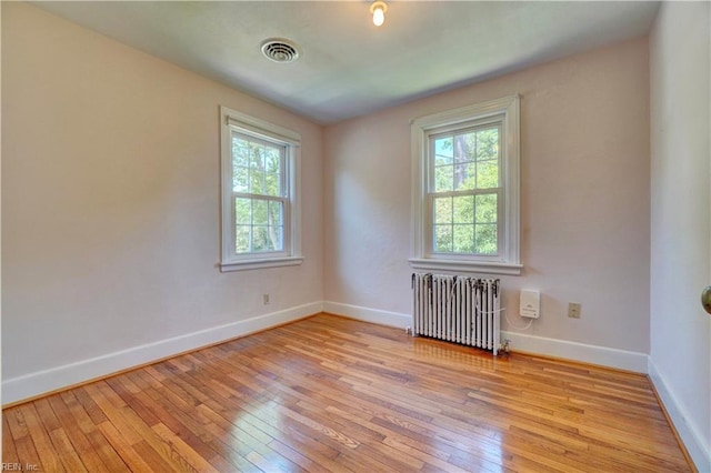 unfurnished room with radiator, healthy amount of natural light, light wood-style floors, and baseboards