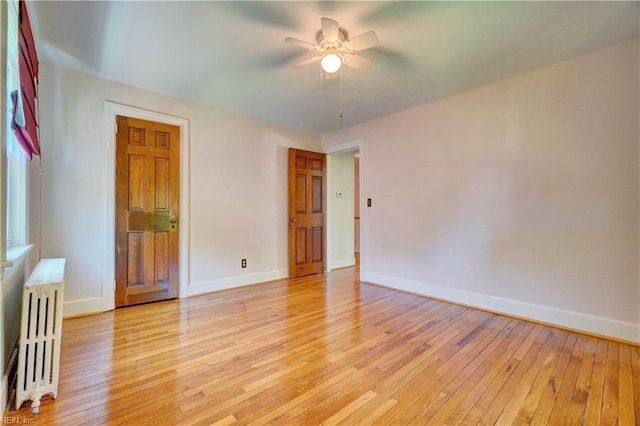 empty room with radiator, ceiling fan, light wood finished floors, and baseboards