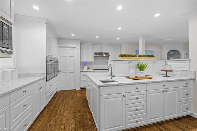 kitchen with appliances with stainless steel finishes, a sink, under cabinet range hood, white cabinetry, and dark wood-style flooring