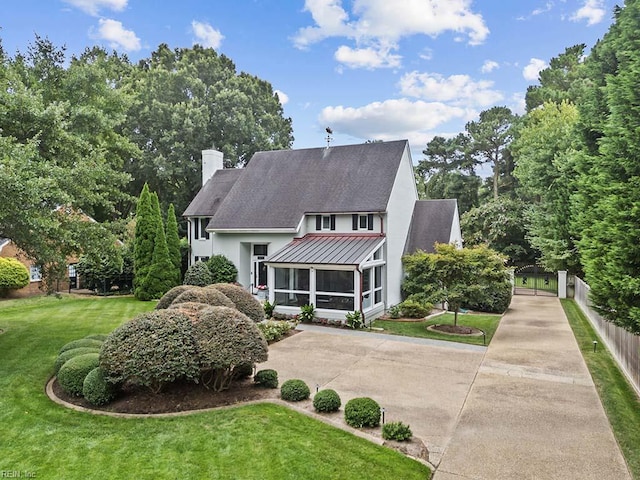 view of front of home featuring a sunroom, a chimney, a shingled roof, driveway, and a standing seam roof