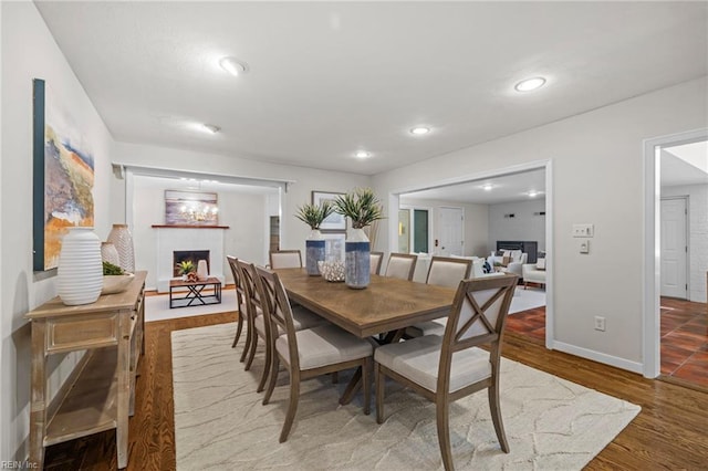 dining area featuring a warm lit fireplace, baseboards, wood finished floors, and recessed lighting