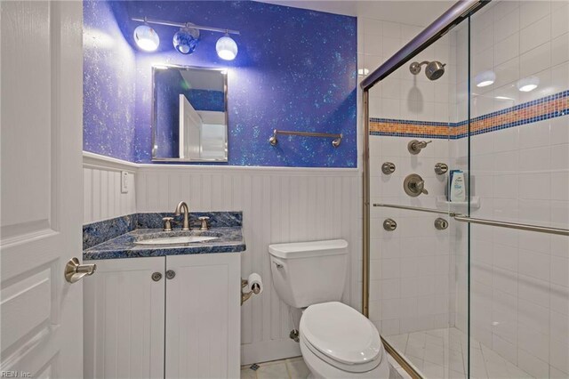 full bathroom featuring toilet, a wainscoted wall, a stall shower, and vanity