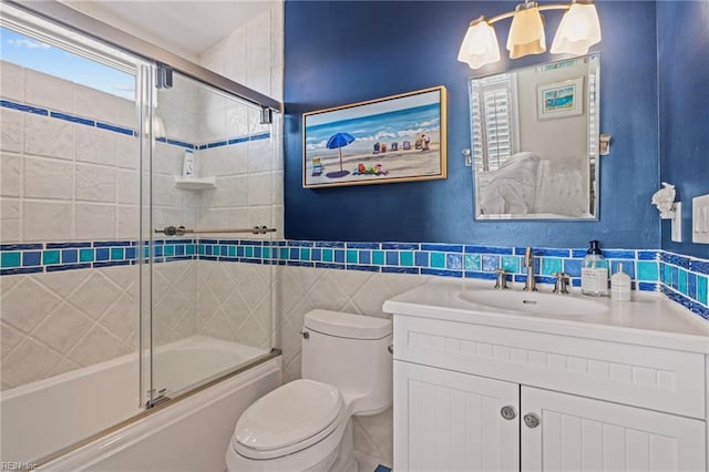 bathroom with toilet, bath / shower combo with glass door, vanity, and tile walls