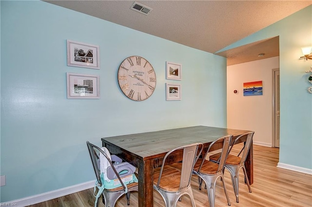 dining space featuring light wood finished floors, baseboards, and vaulted ceiling