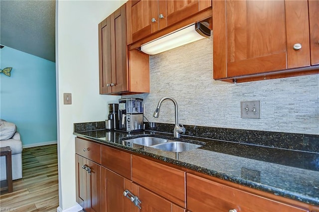 kitchen with a sink, dark stone counters, brown cabinets, and wood finished floors
