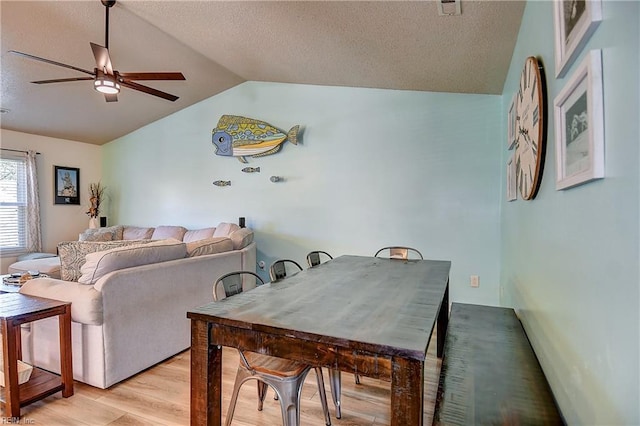 dining area featuring vaulted ceiling, light wood-type flooring, a ceiling fan, and a textured ceiling