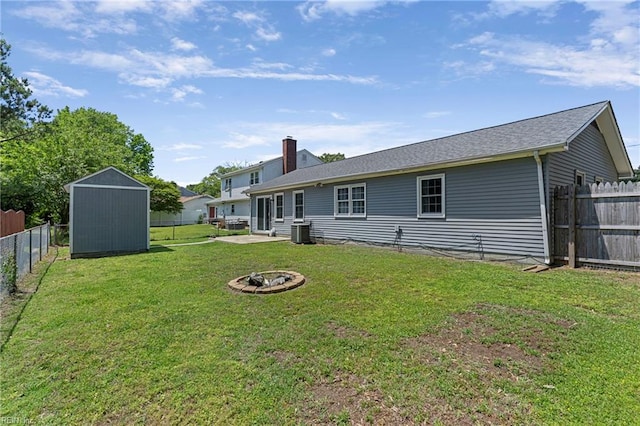 rear view of house with a storage unit, central air condition unit, an outdoor fire pit, an outbuilding, and a chimney