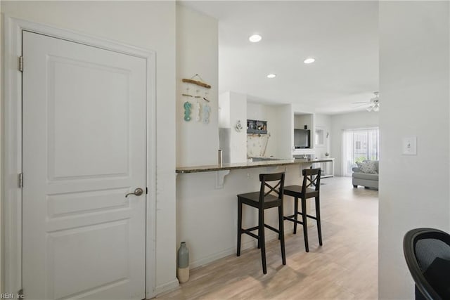 kitchen featuring a kitchen bar, recessed lighting, ceiling fan, dark stone counters, and baseboards