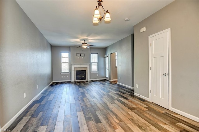 unfurnished living room with ceiling fan, dark wood finished floors, a glass covered fireplace, baseboards, and a chandelier