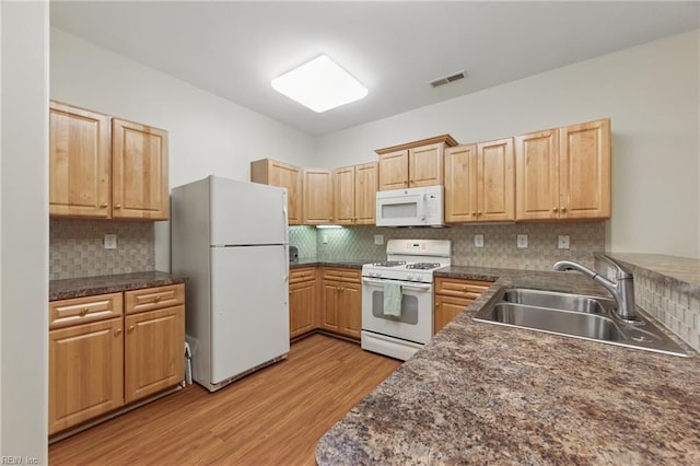 kitchen featuring white appliances, a sink, light wood finished floors, and dark countertops