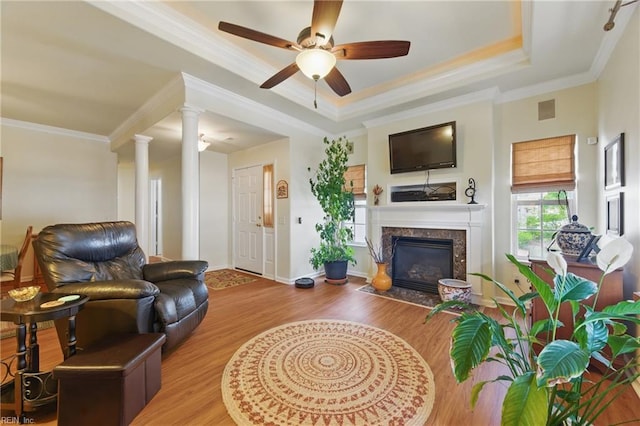 living area with ornate columns, wood finished floors, crown molding, a premium fireplace, and ceiling fan