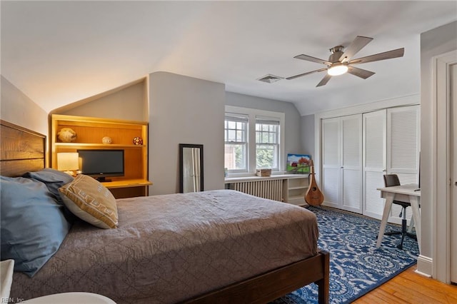 bedroom featuring vaulted ceiling, wood finished floors, a closet, a ceiling fan, and radiator heating unit