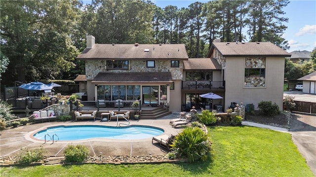 rear view of house featuring a chimney, a balcony, a yard, a patio, and stone siding