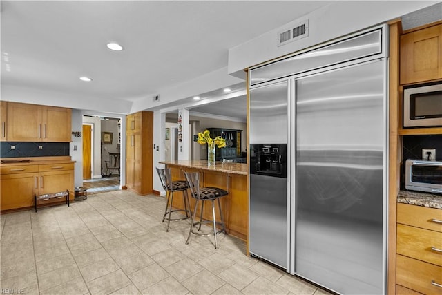 kitchen featuring appliances with stainless steel finishes, recessed lighting, brown cabinetry, tasteful backsplash, and a kitchen breakfast bar