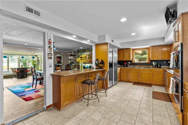 kitchen with appliances with stainless steel finishes, recessed lighting, backsplash, light stone countertops, and a breakfast bar