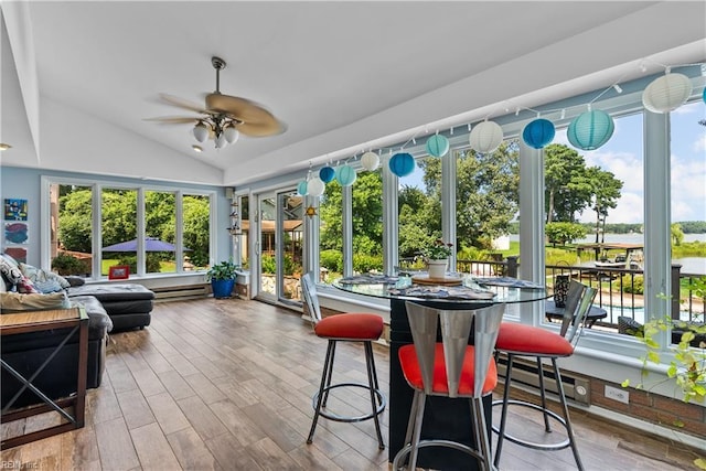 sunroom / solarium with lofted ceiling, plenty of natural light, wood finished floors, and a baseboard heating unit