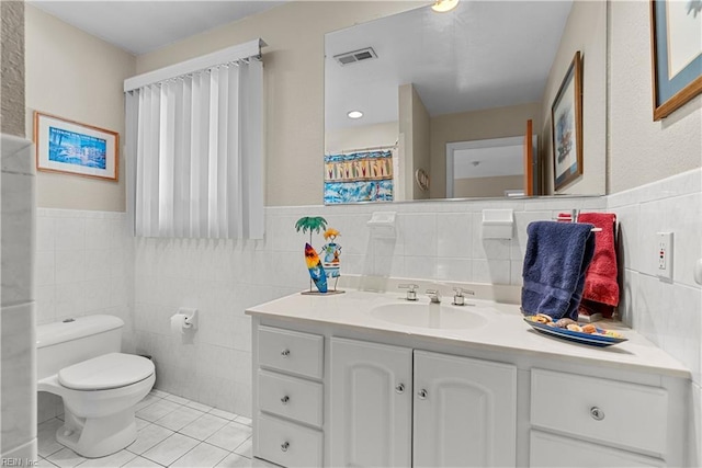 bathroom featuring tile walls, tile patterned floors, toilet, vanity, and a wainscoted wall