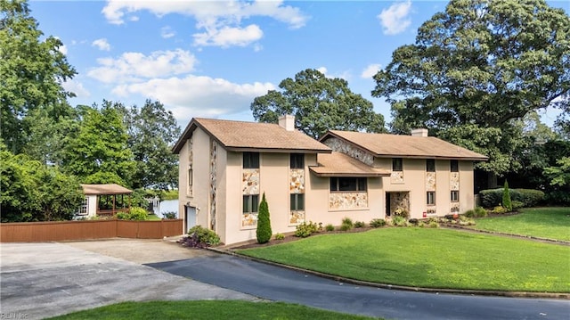 view of front of house featuring asphalt driveway, stone siding, a front yard, stucco siding, and a chimney