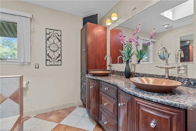 bathroom with a skylight, baseboards, double vanity, tile patterned flooring, and tasteful backsplash