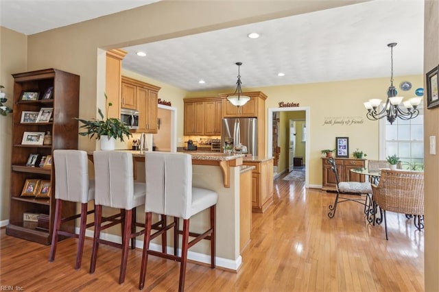 kitchen with appliances with stainless steel finishes, a peninsula, a kitchen bar, light wood-type flooring, and decorative light fixtures