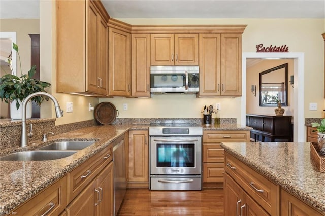 kitchen with appliances with stainless steel finishes, a sink, stone countertops, wood finished floors, and brown cabinets
