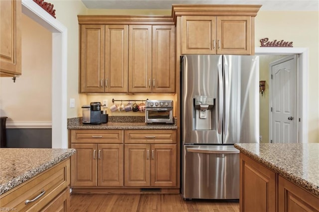 kitchen featuring stainless steel refrigerator with ice dispenser, light stone counters, light wood-style flooring, and brown cabinets