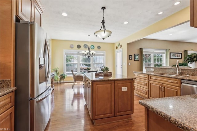 kitchen with appliances with stainless steel finishes, a sink, wood finished floors, a center island, and a chandelier