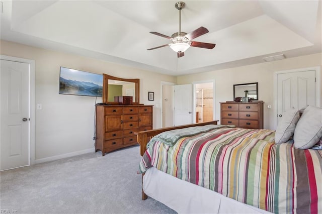 bedroom with a tray ceiling, carpet, baseboards, ceiling fan, and ensuite bath