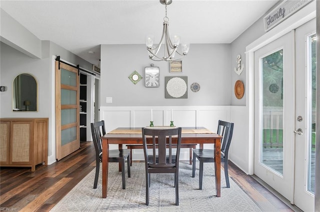 8209 Harlan Dr, Suffolk, VA 23436 - dining space with a barn door, wood finished floors, a chandelier, a wainscoted wall, and a decorative wall