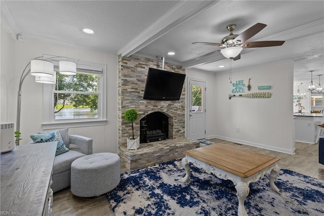 living room with a textured ceiling, wood finished floors, ornamental molding, a ceiling fan, and a stone fireplace